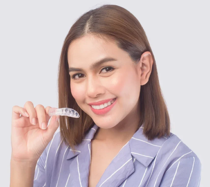 Smiling patient holding a clear Invisalign aligner — Brace Central Orthodontics, Brooklyn
