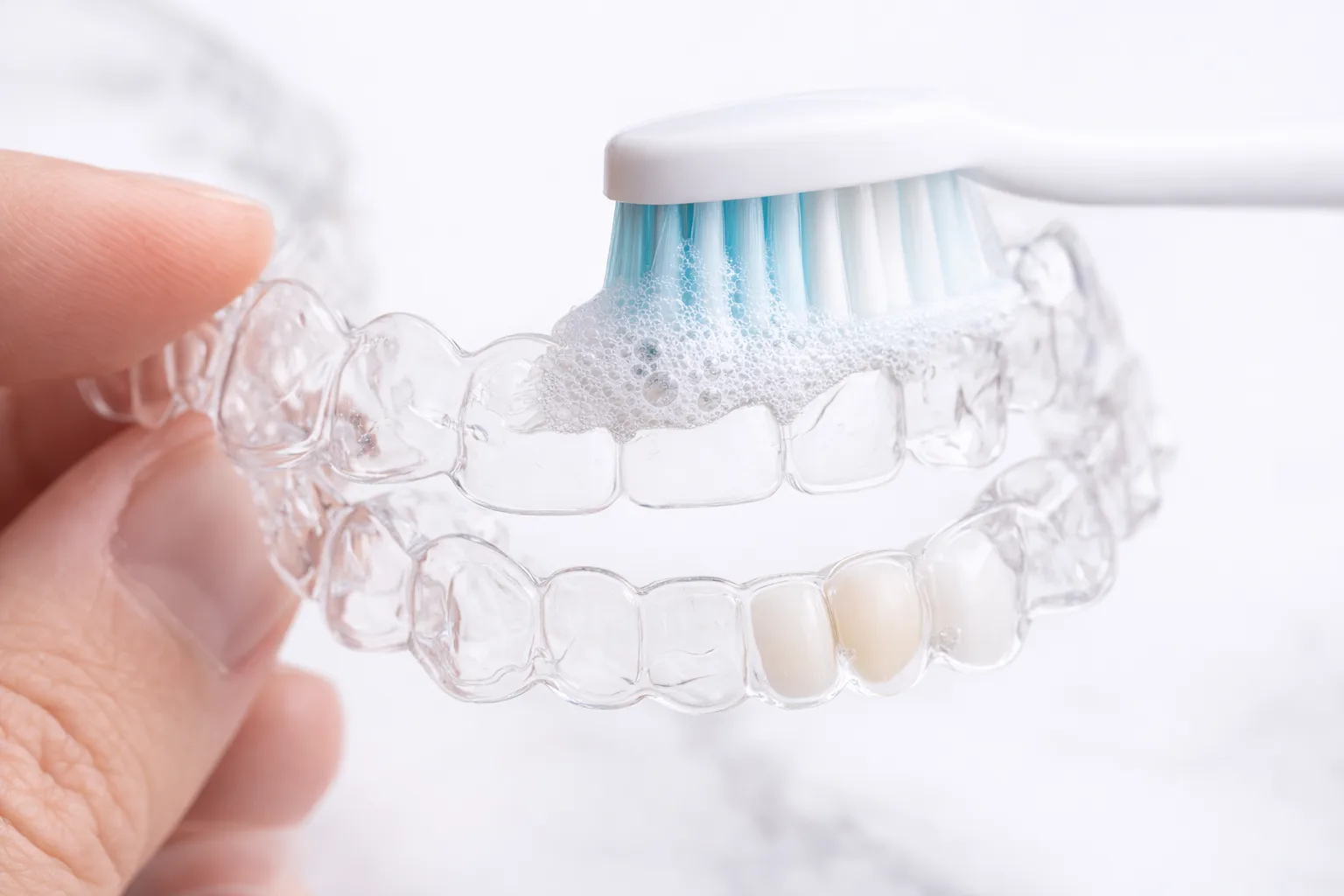 Gently brushing a clear Invisalign aligner with a soft toothbrush and soap to keep it clean