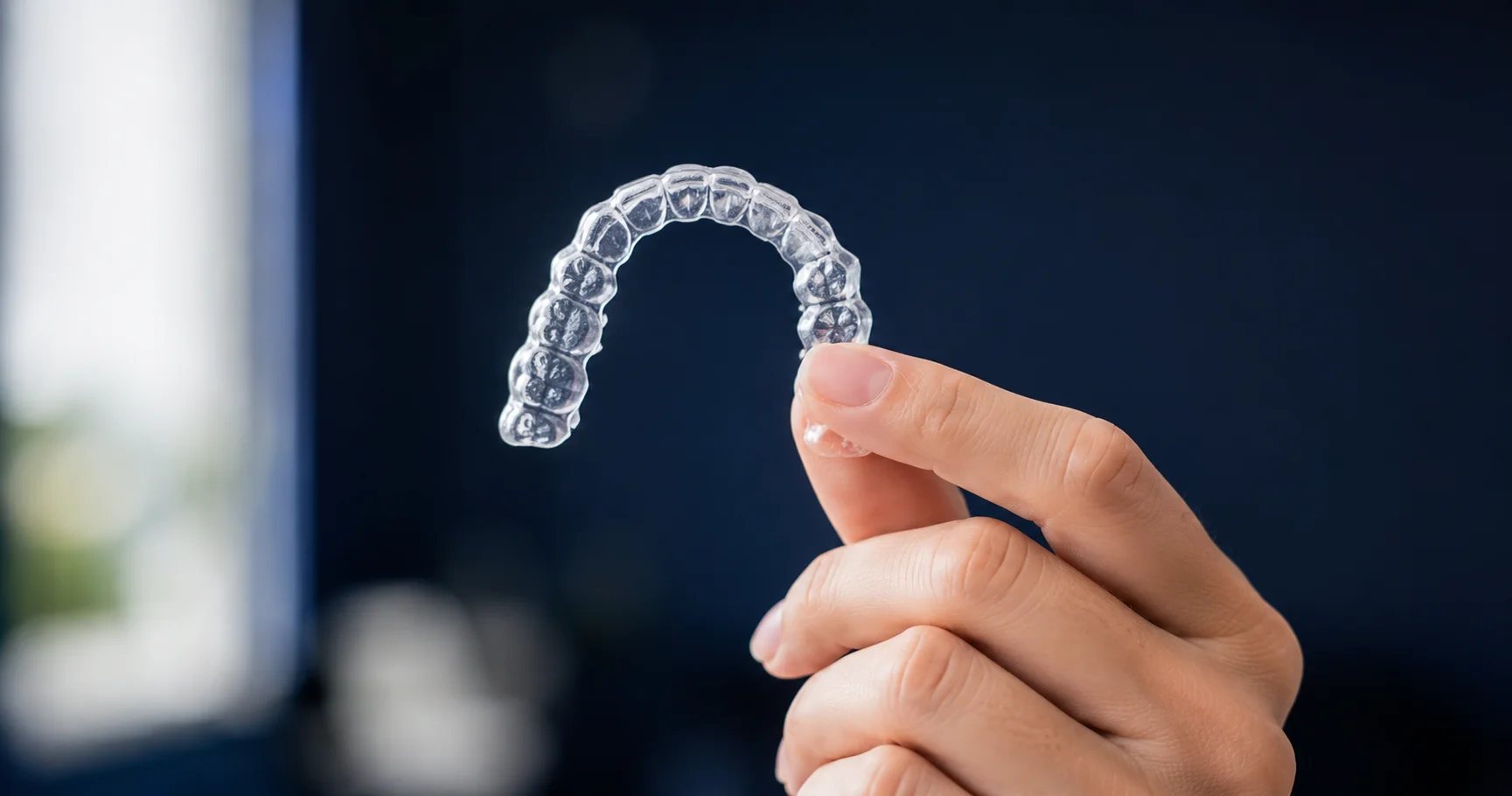 Clear Invisalign aligner held between fingers, showing a removable orthodontic option from a Brooklyn orthodontist